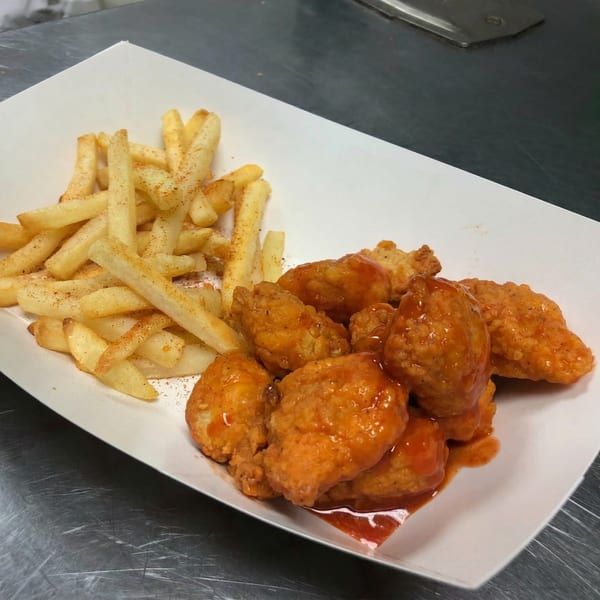 Crispy french fries seasoned with paprika next to saucy boneless buffalo wings in a white paper tray.