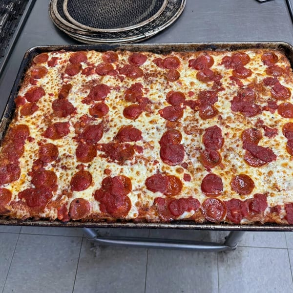 A rectangular pepperoni pizza with melted cheese and red sauce on a dark baking sheet.