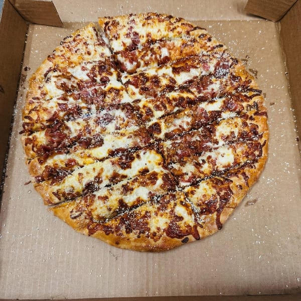 A whole, sliced pizza with white cheese, bacon, and a dark sauce in a cardboard box.