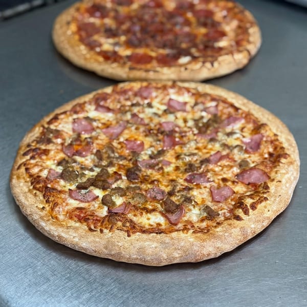 Two freshly baked pizzas, one with pepperoni and the other with sausage and ham, on a metal surface.