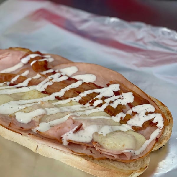 Open-faced sub sandwich with ham, melted cheese, bacon bits, and white sauce on foil.
